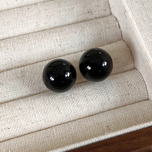 Close-up of polished black spherical stud earrings in a beige velvet jewelry box display