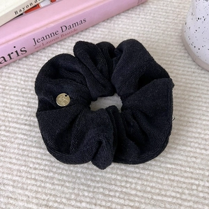 Detail of black scrunchie in bouclé fabric with a round gold engraved metal charm