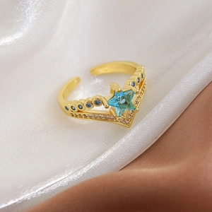 Macro detail of V-shaped gold ring with blue star gemstone and micro-pave crystals