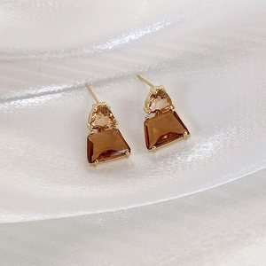 Detail of amber crystal geometric earrings on white silk fabric highlighting golden claws
