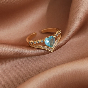 Detail of gold open ring featuring a blue heart gemstone and V-shaped pavé setting