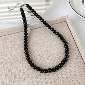 Detail of black glass beaded necklace with silver lobster clasp on a beige linen tray