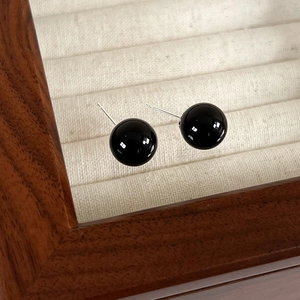 Close-up of minimalist black spherical stud earrings set in a premium velvet jewelry box