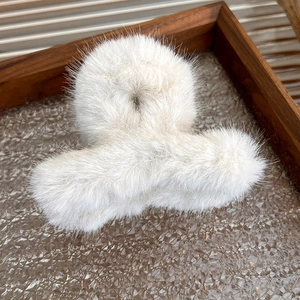 Detail of soft white plush claw clip on vintage wooden tray with textured glass background