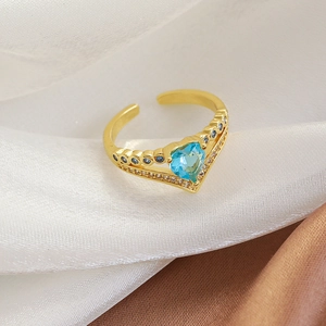 Macro shot of gold V-shaped open ring with heart blue zircon on silk fabric