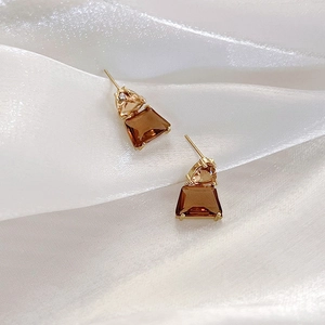 Macro shot of French caramel crystal geometric earrings on white silk fabric background