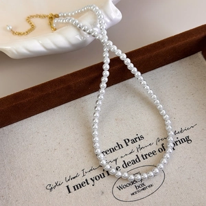 Detail of white faux pearl necklace with gold lobster clasp on a beige display board