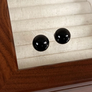 Macro shot of minimalist black bead earrings on a wooden jewelry box with fabric lining