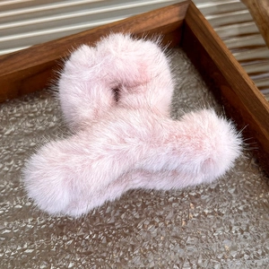 Close-up of soft pink faux fur hair claw clip on a rustic wooden tray with art glass