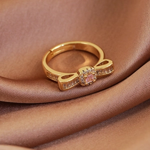Macro view of gold bow-shaped open ring with pink gemstone on brown silk background