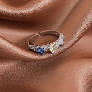 Close-up of silver open ring with heart and rectangle gemstones on red silk fabric