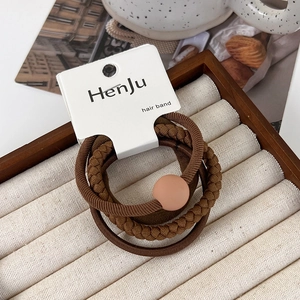 Three deep brown hair ties featuring smooth beads and woven textures on a display card