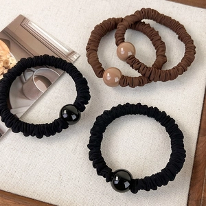 Détail de trois élastiques à cheveux noirs et marrons avec de grandes perles polies