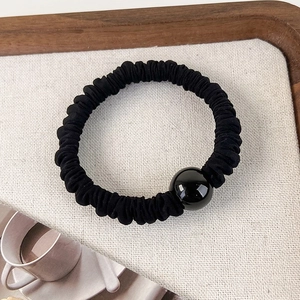 Détail d'un chouchou élastique noir avec une grande perle noire polie sur un plateau
