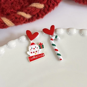 Detail of Christmas asymmetric earrings featuring a snowman and candy cane on ceramic plate