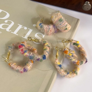Détail de boucles d'oreilles créoles en laine tricotée colorée sur fond de livre Paris