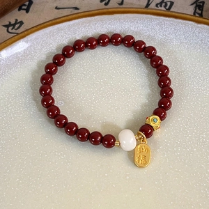 Detail of red beaded bracelet with golden Nafu charm and white bead on ceramic tray
