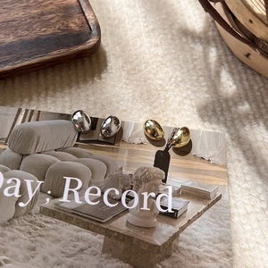 Polished gold and silver bean-shaped minimalist stud earrings set on a magazine background