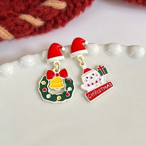 Macro detail of asymmetric Christmas wreath and snowman stud earrings on a ceramic tray