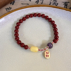 Macro shot of red beaded bracelet featuring a golden lucky charm on a ceramic plate