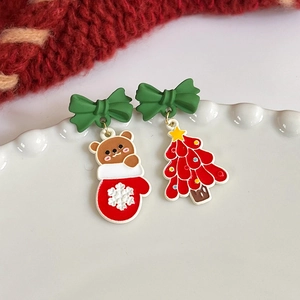 Detail of asymmetric Christmas earrings with cartoon bear and festive tree on a white plate