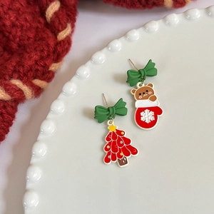 Detailed view of asymmetric Christmas earrings featuring a festive tree and bear on a plate