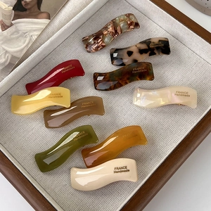 French style wavy acetate hair clips in multiple colors on a cream display tray