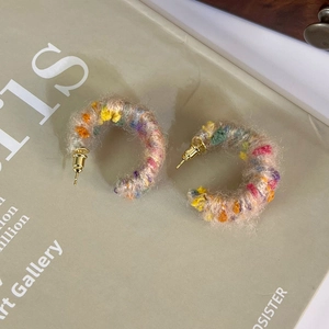 Gros plan de boucles d'oreilles créoles C en peluche colorée avec texture tricotée et clous dorés