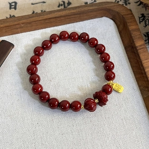 Detail of red beaded bracelet featuring a lotus bead and golden Fu character charm