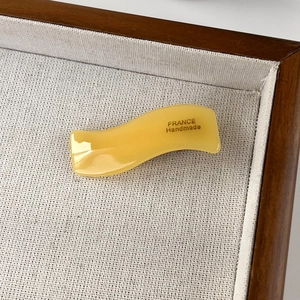 Detailed macro view of yellow wavy acetate hair clip with FRANCE Handmade engraving