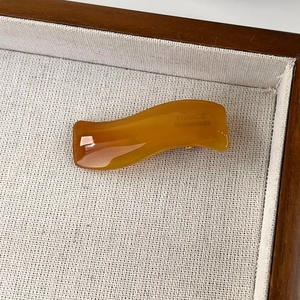 Detail showing amber wavy acetate hair clip with gold France Handmade logo on linen