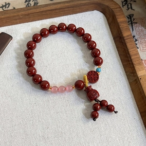 Detail of red beaded bracelet featuring a luck pouch charm and coin pendant in wood tray