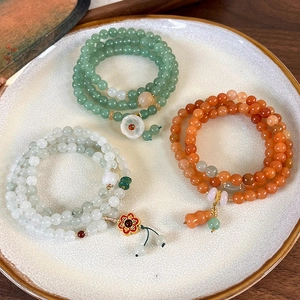 Detail view of multi-layered green agate beaded bracelets with floral pendants in a ceramic tray