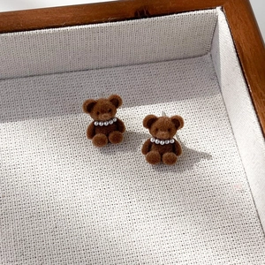 Makroaufnahme brauner beflockter Bärenohrringe mit Perlenhalsband auf Holztablett