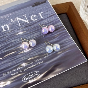 Macro detail of three pairs of pearlescent studs in light purple, pink, and blue shades