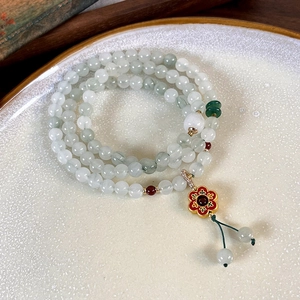 Detailed macro of multi-layer jade bead bracelet featuring a red enamel flower pendant