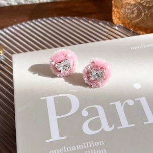 Détail de boucles d'oreilles peluche rose avec nœud en cristal et perles sur livre