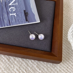 Close-up of luxury iridescent pearl stud earrings on a grey minimalist display base