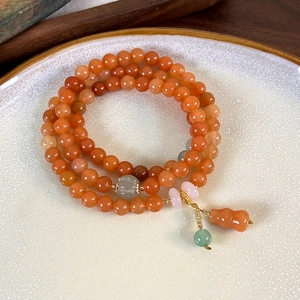 Detail of multi-layer orange agate bead bracelet with gourd pendant on white ceramic plate