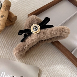 Macro detail of plush brown hair claw with velvet bow and pearl camellia charm