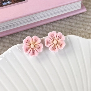 Close-up of pink cherry blossom stud earrings with velvet texture in a shell dish