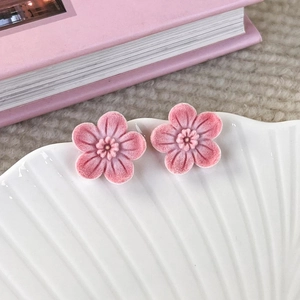 Detailed close-up of pink flocked cherry blossom stud earrings on a white shell tray