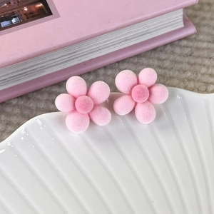 Close-up of pink fuzzy flower stud earrings with soft flocking texture on a white plate