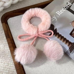 Dettaglio di un elastico per capelli in finta pelliccia rosa con pompon a forma di ciliegia