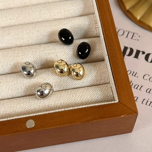 Detailed macro view of minimalist oval stud earrings in black, gold, and silver finishes