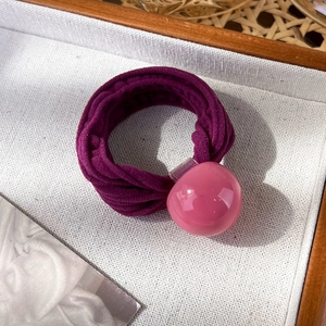 Gros plan d'un élastique à cheveux violet avec une perle acrylique rose sur un plateau