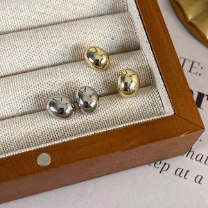 Polished pebble-shaped stud earrings in gold and silver set in a linen jewelry box