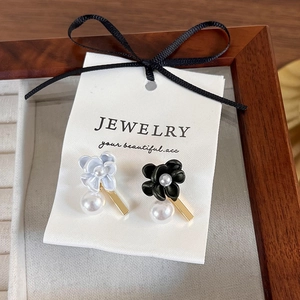 Detail of asymmetric gardenia flower earrings with pearls on jewelry display card
