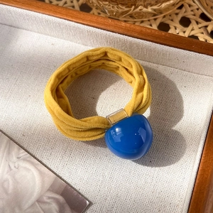Détail d'un chouchou en tissu jaune gingembre avec perle en résine bleue dans un plateau
