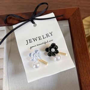 Close-up of asymmetrical black and white floral pearl earrings on a display card